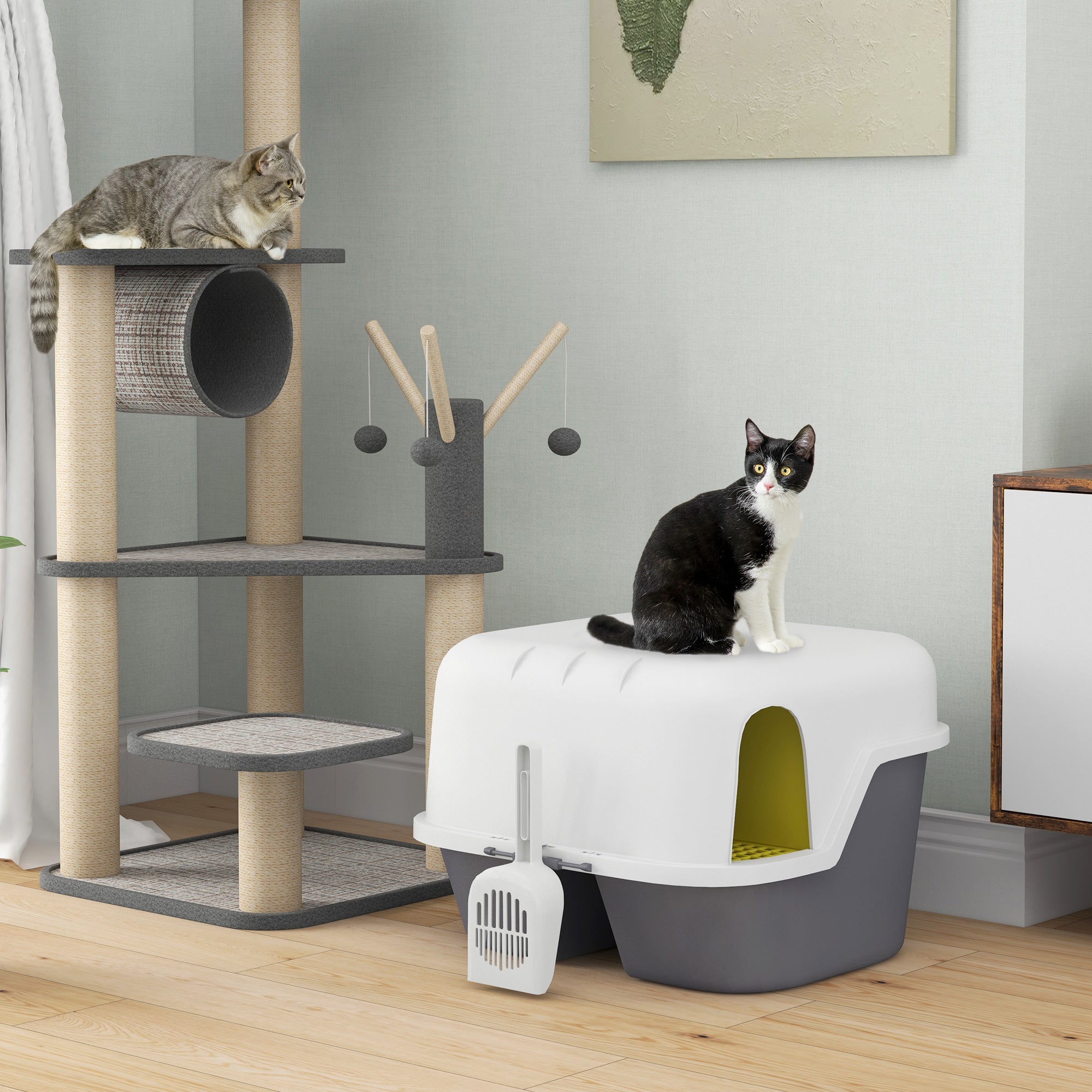 En svartvit katt står bredvid en elegant halvöppen kattlåda i cremévitt och grått med integrerad sandfångare, placerad på ett trägolv.