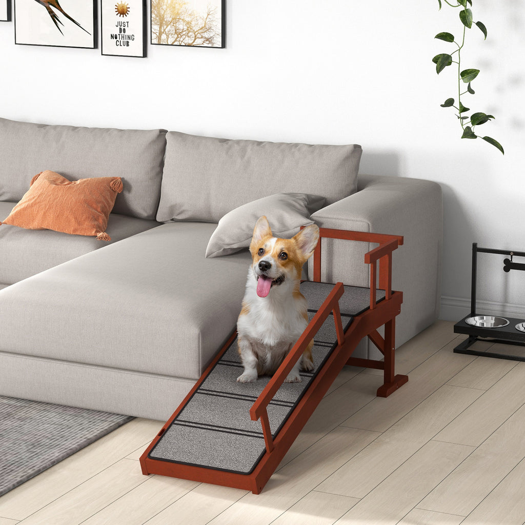 En liten hund går tryggt uppför en stabil hundramp i trä placerad vid en grå soffa.