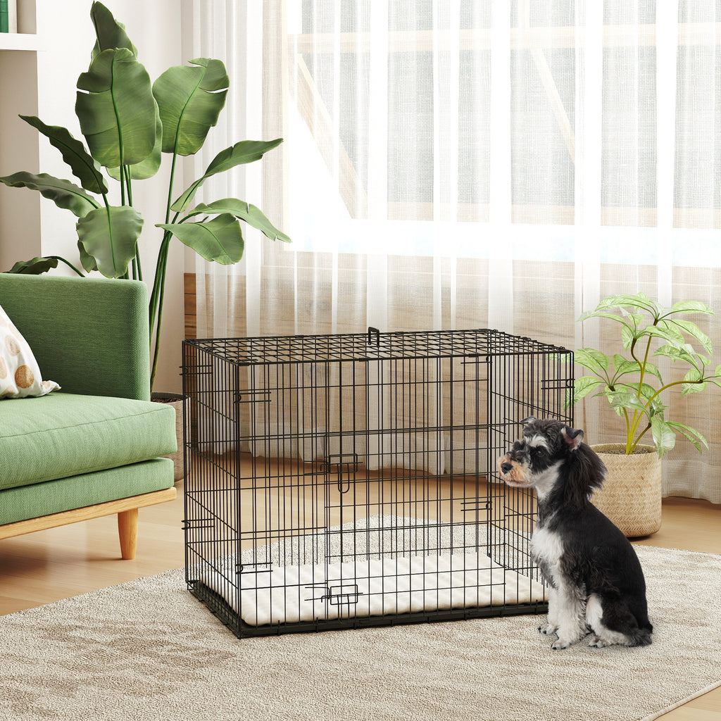 Svart hundbur i ståltråd med mjuk beige dyna placerad i ett vardagsrum med en liten hund
