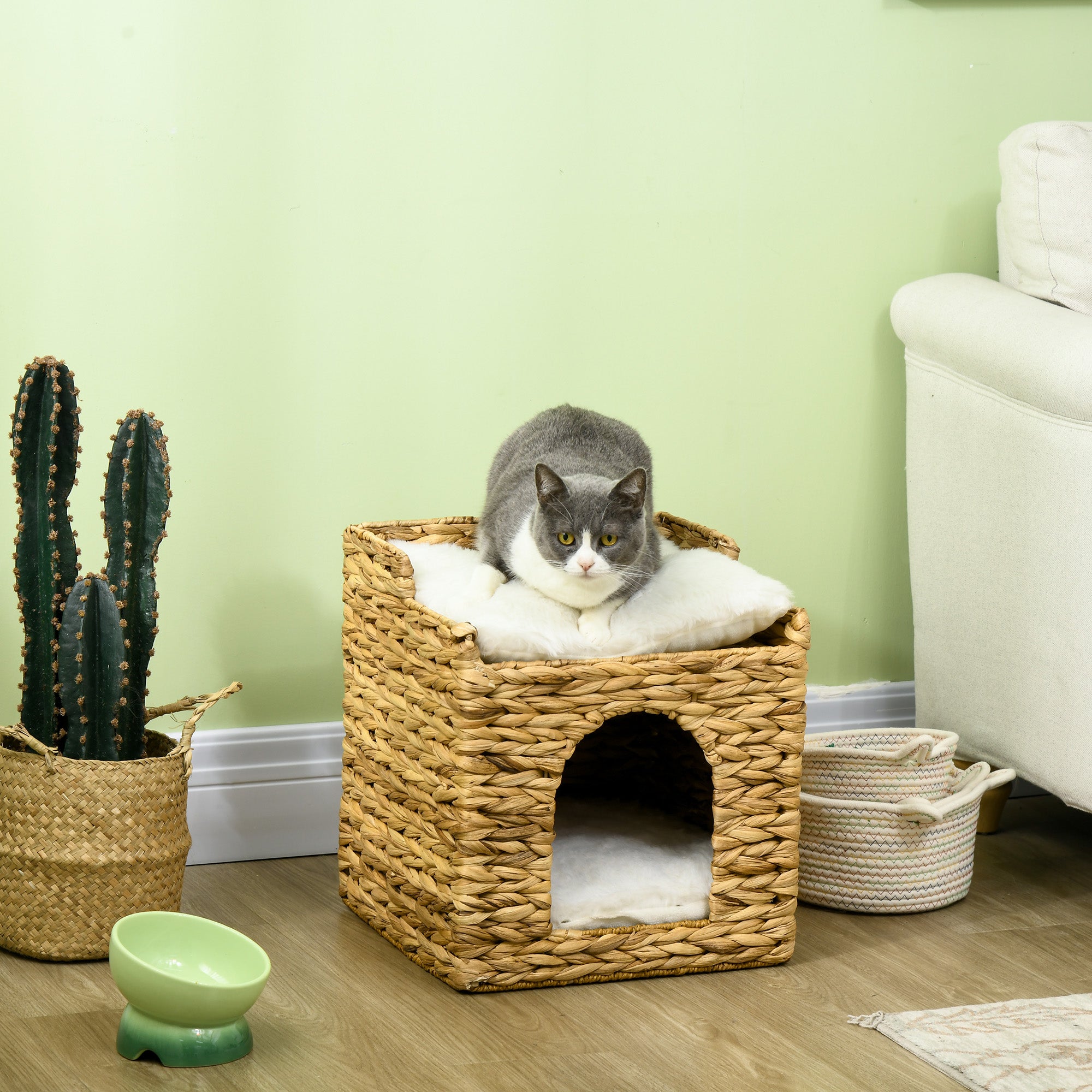 Ett elegant handflätat katthus i vattenhyacint med två nivåer och mjuka vita plyschkuddar där en katt vilar tryggt.