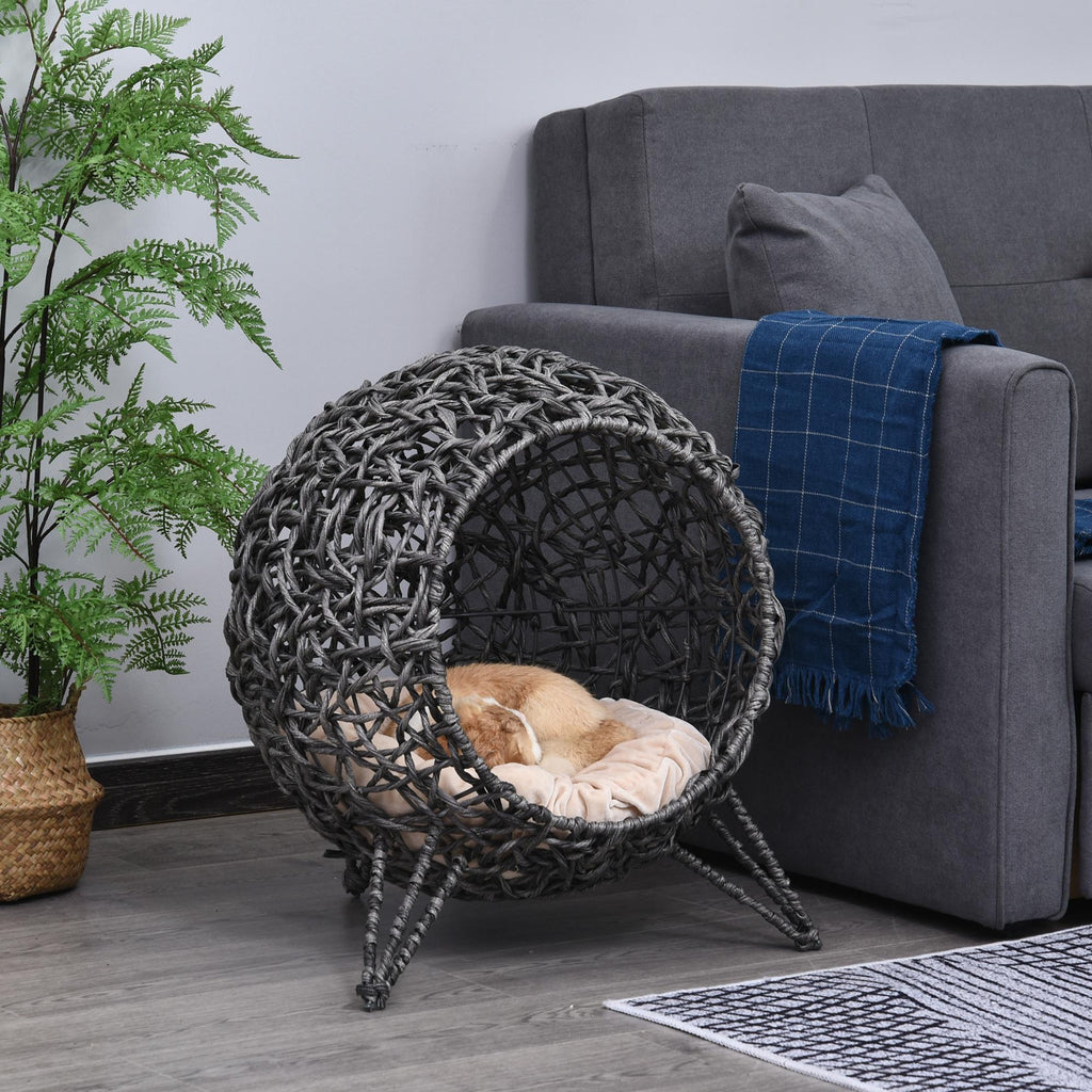 Modern rund kattgrotta i silvergrå rottingstil placerad vid en soffa.