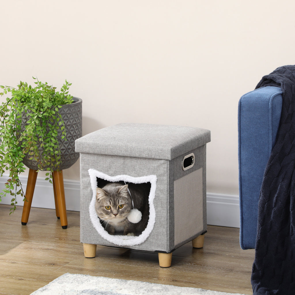 En modern grå och cremevit kattgrotta som även fungerar som en sittpuff, med kattformad öppning, leksaksboll och sisalyta på sidan.