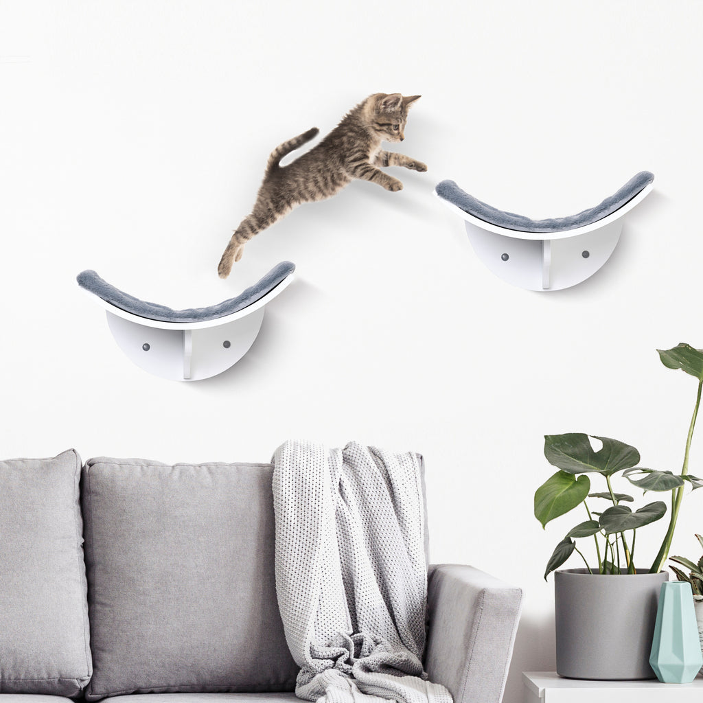 En stilren väggmonterad kattbädd i grå plysch med en vit katt som hoppar upp på den.